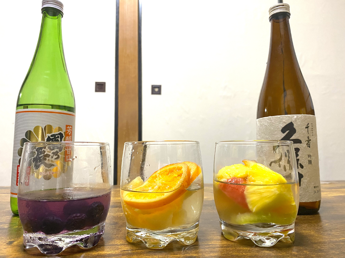 フルーツと日本酒が入ったグラスと日本酒の瓶2本