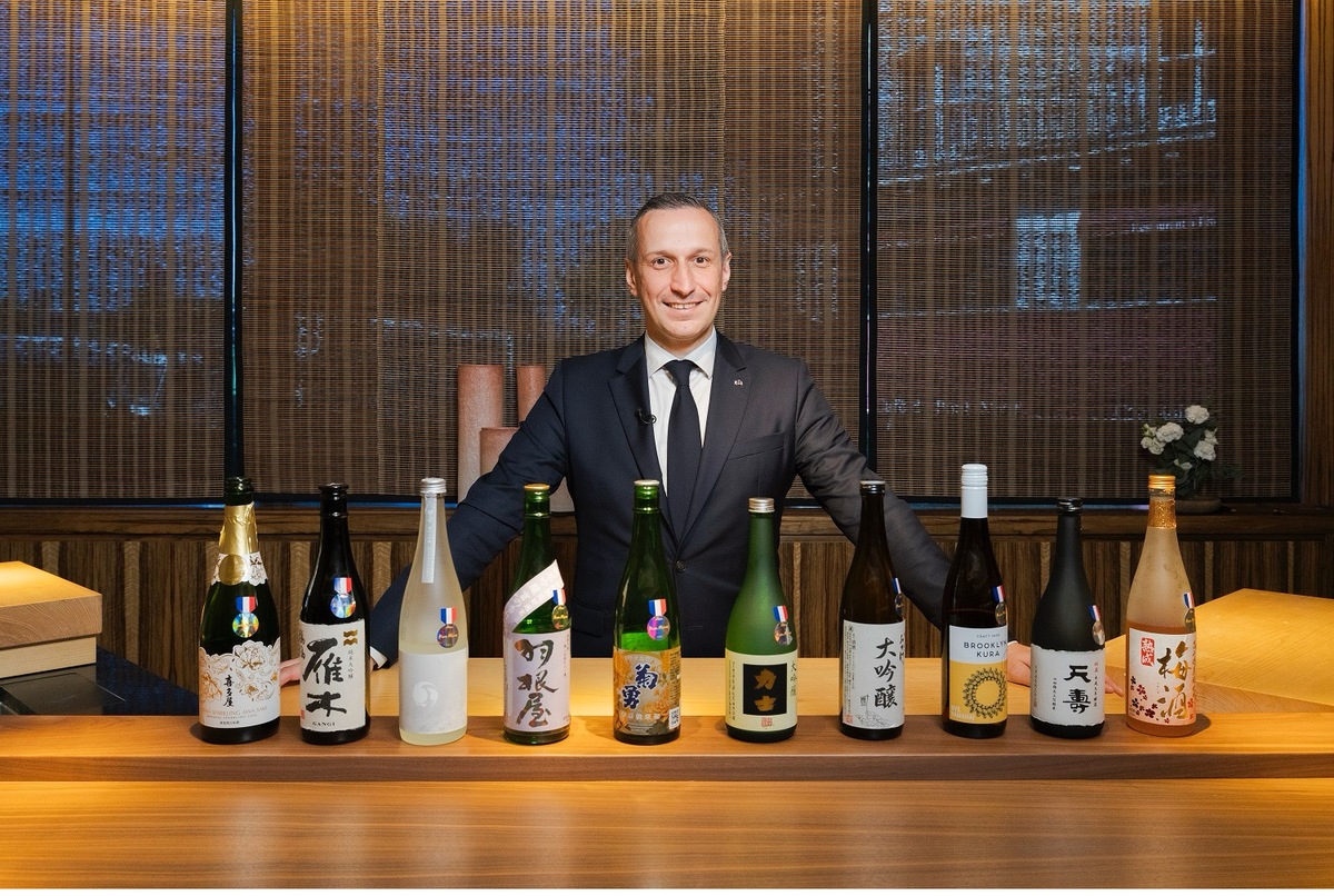 日本酒の瓶を並べ、手を広げる男性