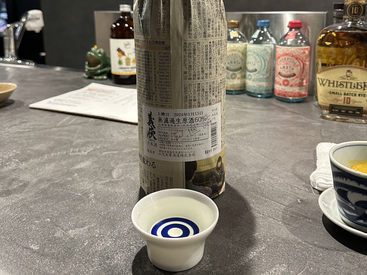 新聞紙にくるまれた日本酒の瓶とお猪口