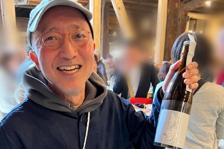 日本酒の瓶を手に笑顔を見せる男性