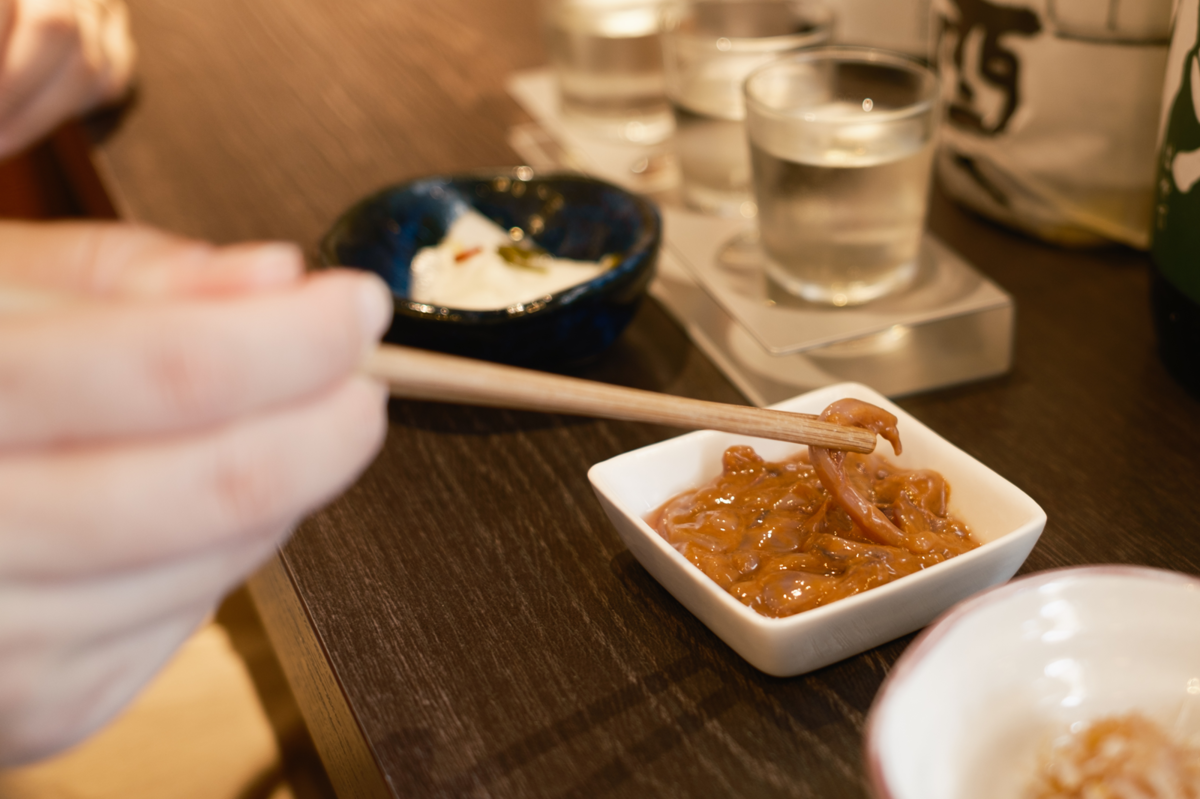 日本酒とともにイカの塩辛をいただく女性の手元