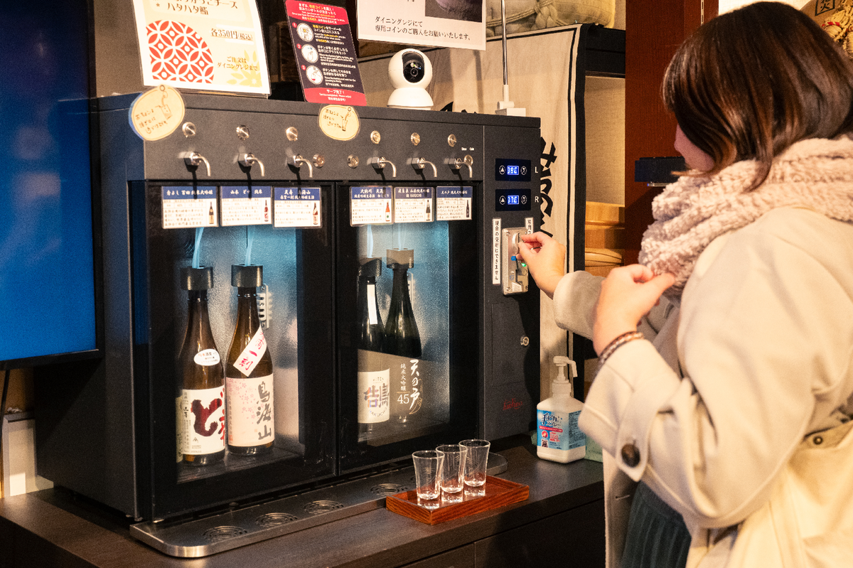 日本酒の試飲器にコインを投入する女性